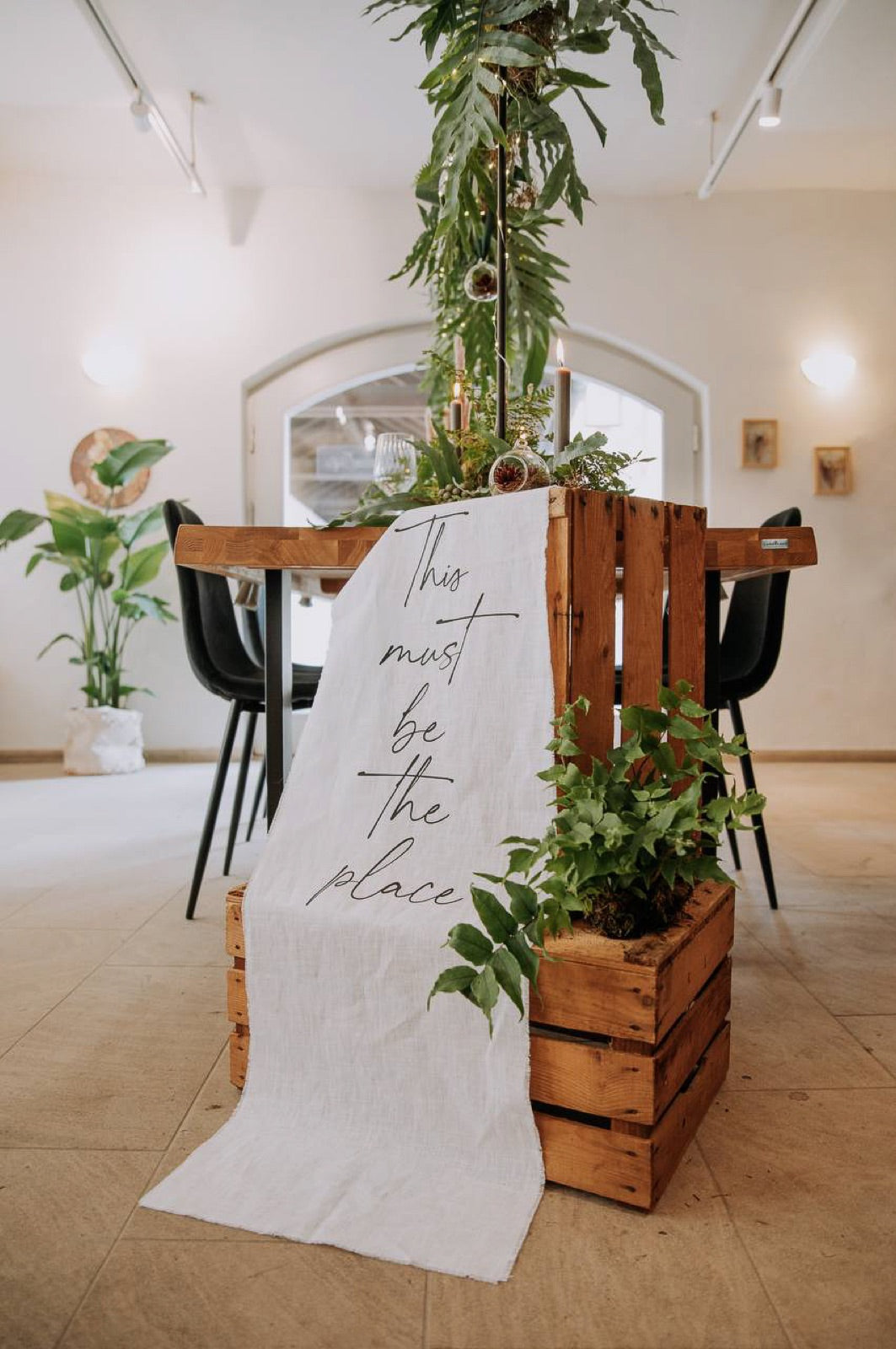 Tischläufer aus Leinen mit Schriftzug „This must be the place“ auf Holzkiste mit Pflanzen