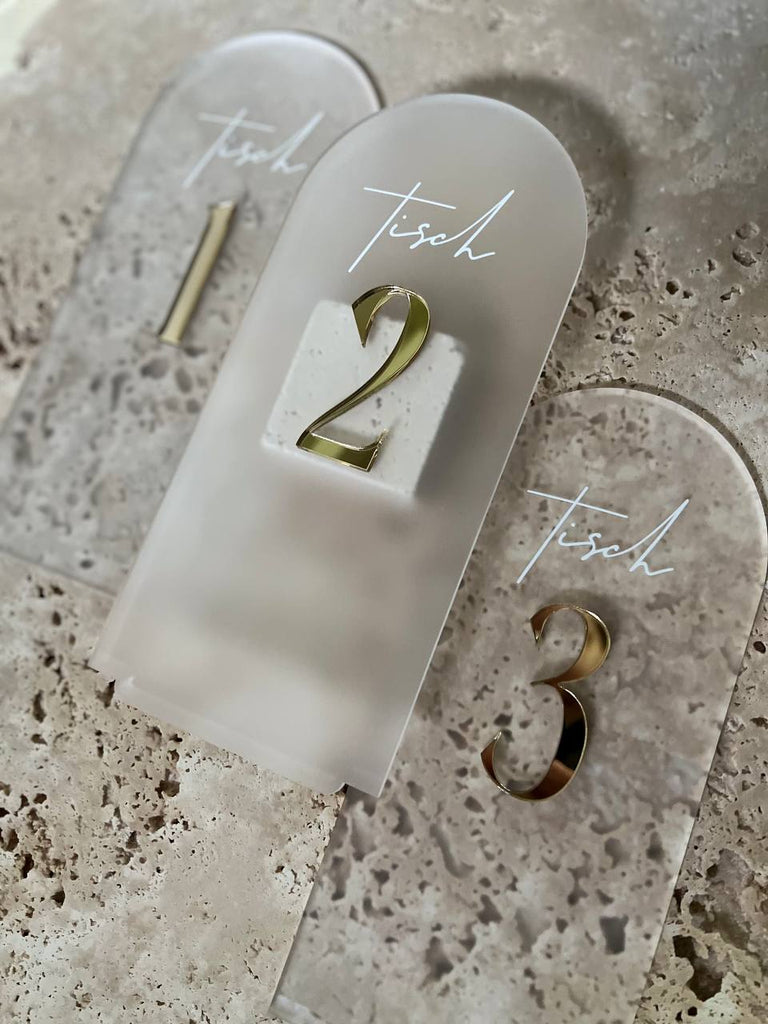 Drei satinierte Acryl-Tischnummern mit goldenen 3D-Zahlen 1, 2 und 3 auf einer Travertinplatte