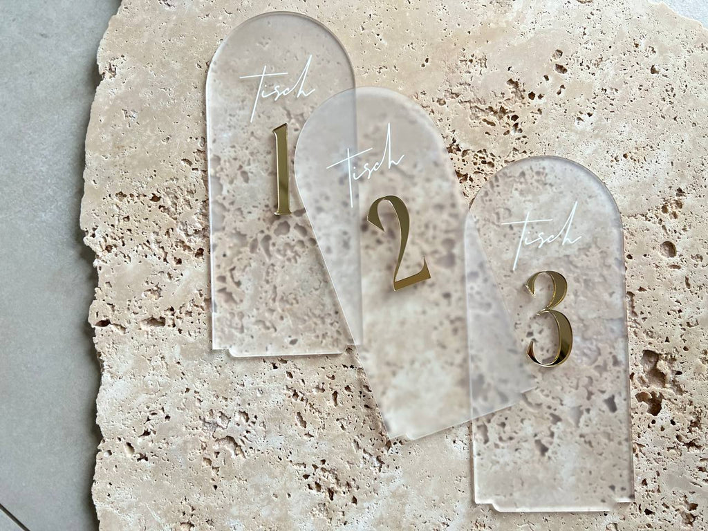Drei halbrunde Tischnummern aus satiniertem Acryl mit goldenen 3D-Zahlen 1 bis 3, überlappend auf Travertinstein arrangiert