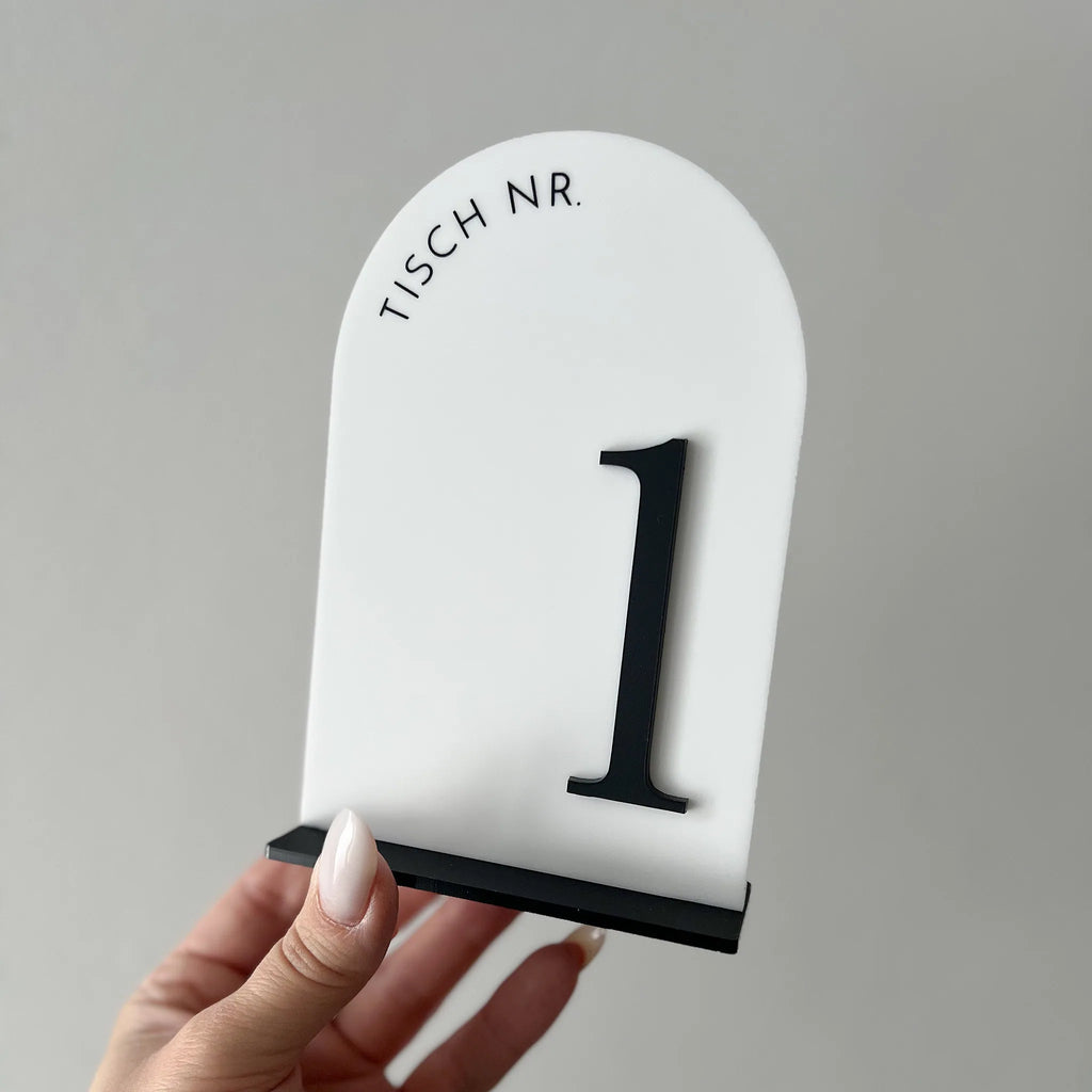 Hand hält weiße Tischnummer in Bogenform mit schwarzer 3D-Zahl 1 und Schriftzug Tisch Nr.