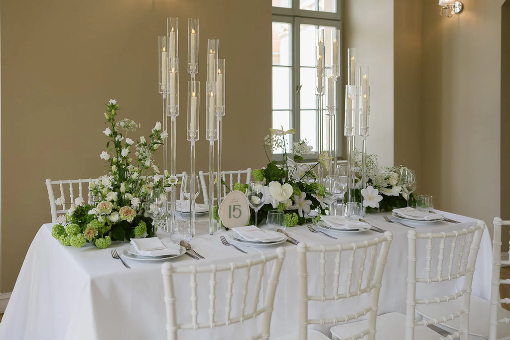 Langer Hochzeitstisch mit hohen Kerzenständern, weißen Blumen und Tischnummer aus Acryl im Zentrum