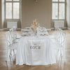 Gedeckter Hochzeitstisch mit weißem Stoffbanner Table Four, das über die Tischkante fällt, umgeben von weißen Stühlen und Kerzenlicht