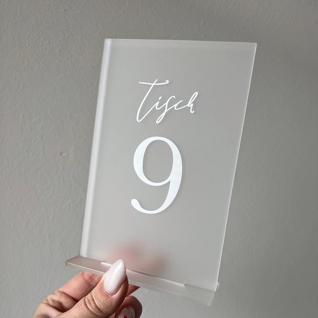 Hand hält eine satinierte Acrylglas-Tischnummer mit weißem Aufdruck Tisch 9 vor grauer Wand