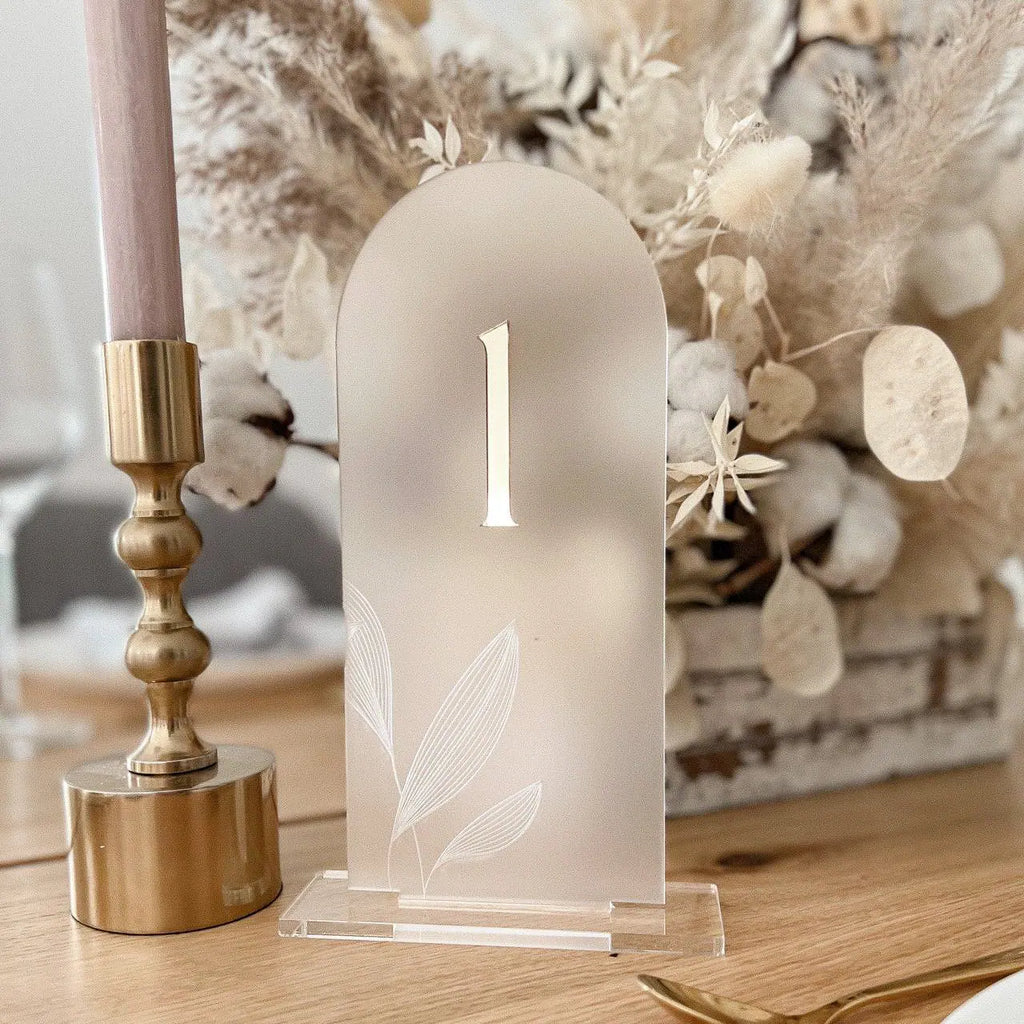 Tischnummer aus satiniertem Acryl mit goldener 3D-Zahl 1 und Blattgravur neben goldenem Kerzenhalter