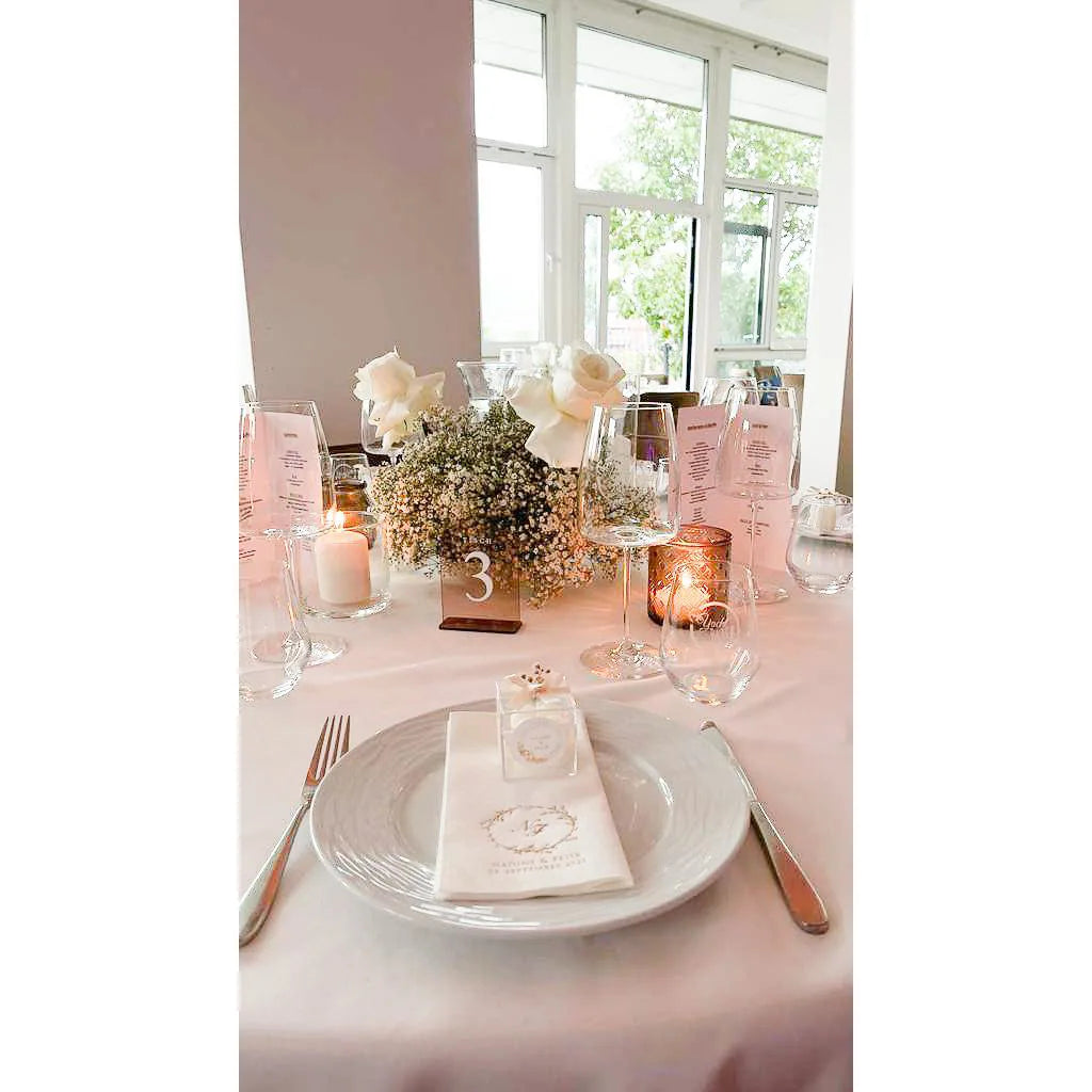 Hochzeitstisch mit rosafarbener Tischdecke, Acrylglas-Tischnummer 3, Kerzen und Blumenstrauß aus Rosen und Schleierkraut.